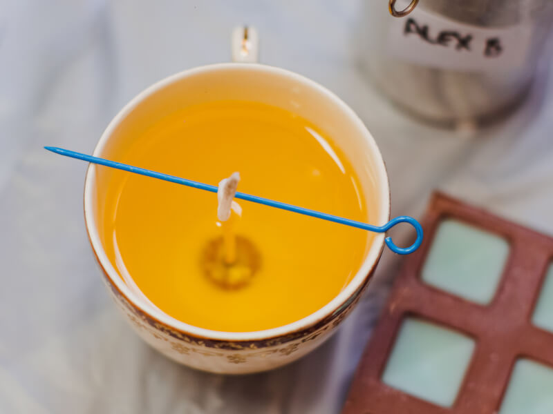 Close up of yellow melted candle wax in a teacup with a blue candle wick holder
